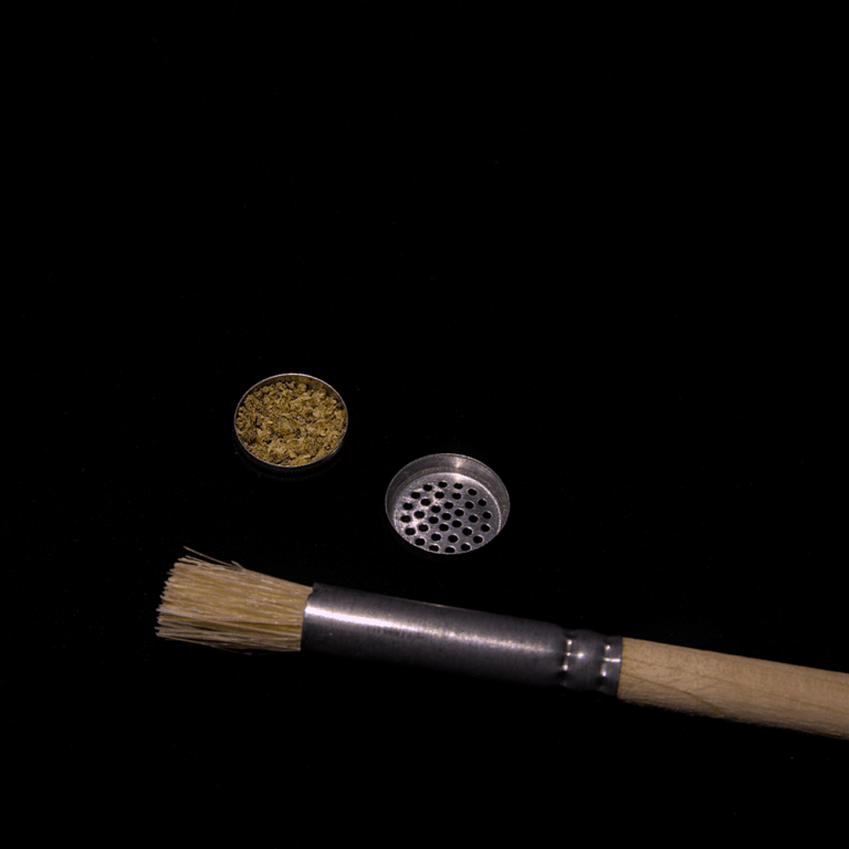 Dosing Capsule containing ground cannabis flower alongside a cleaning brush